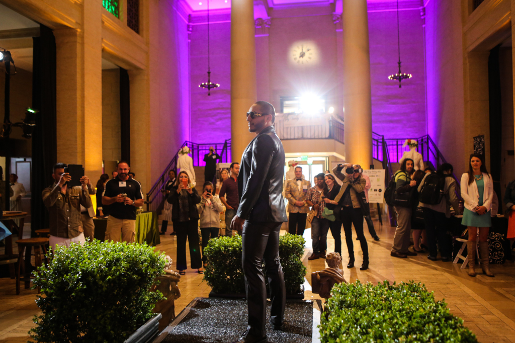Groom model for the vanity wedding show on runway with crowd, in front of purple wall lighting in the background
