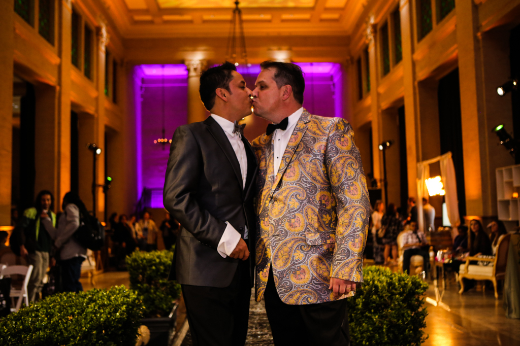 Two men kissing on runway with gold lighting for gay vanity wedding show