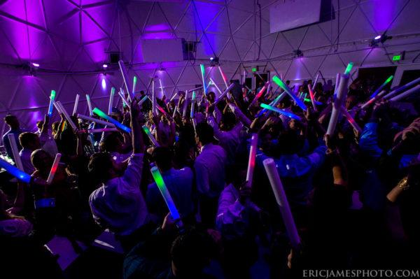 Crowd with glow sticks dancing inside a multicolored dome
